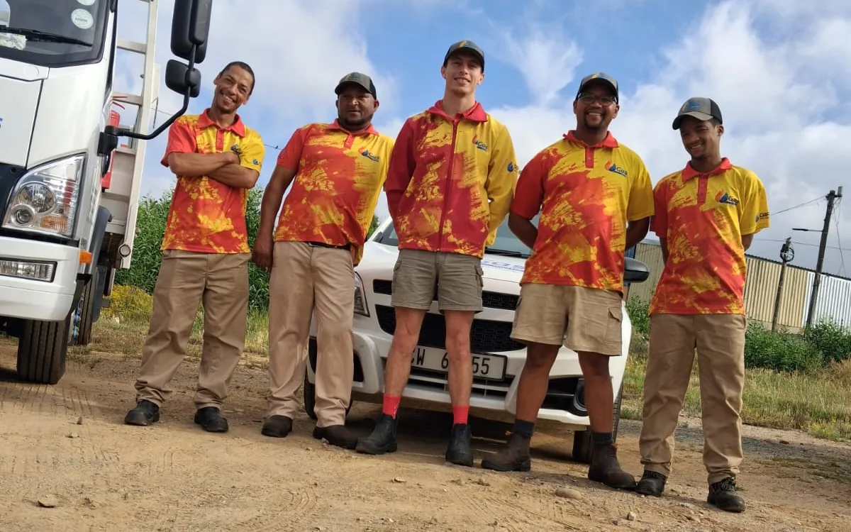 Five WF Gas team members in red and yellow uniforms standing in front of a company car, beside the gas truck