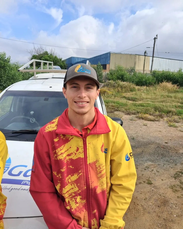 A WF Gas team member in a red and yellow WF Gas jacket beside a company car